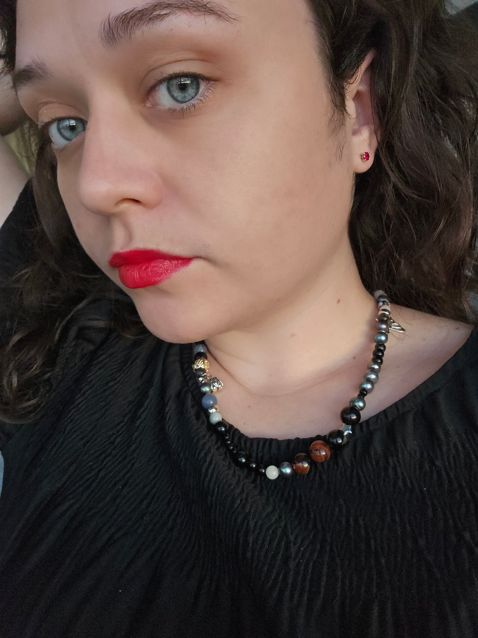 Close-up of a person with red lipstick and black hair, wearing a beaded necklace.