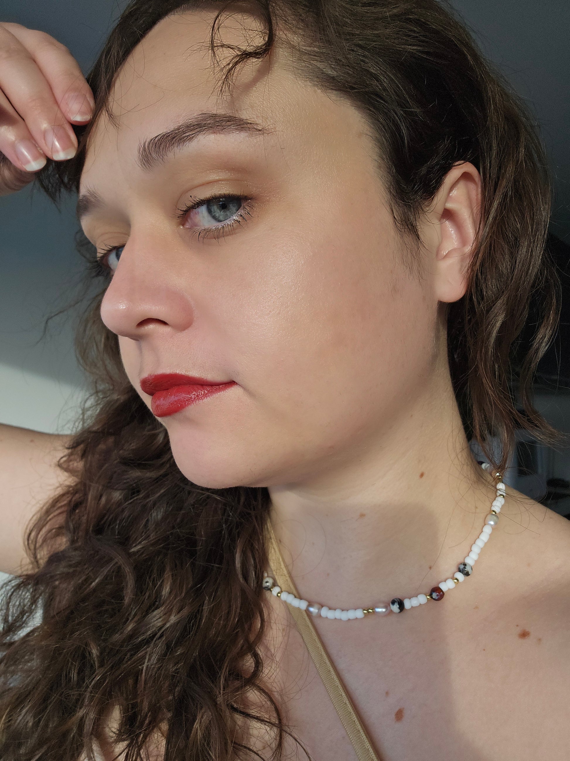 Close-up of a woman with wavy hair and red lipstick, wearing a necklace.