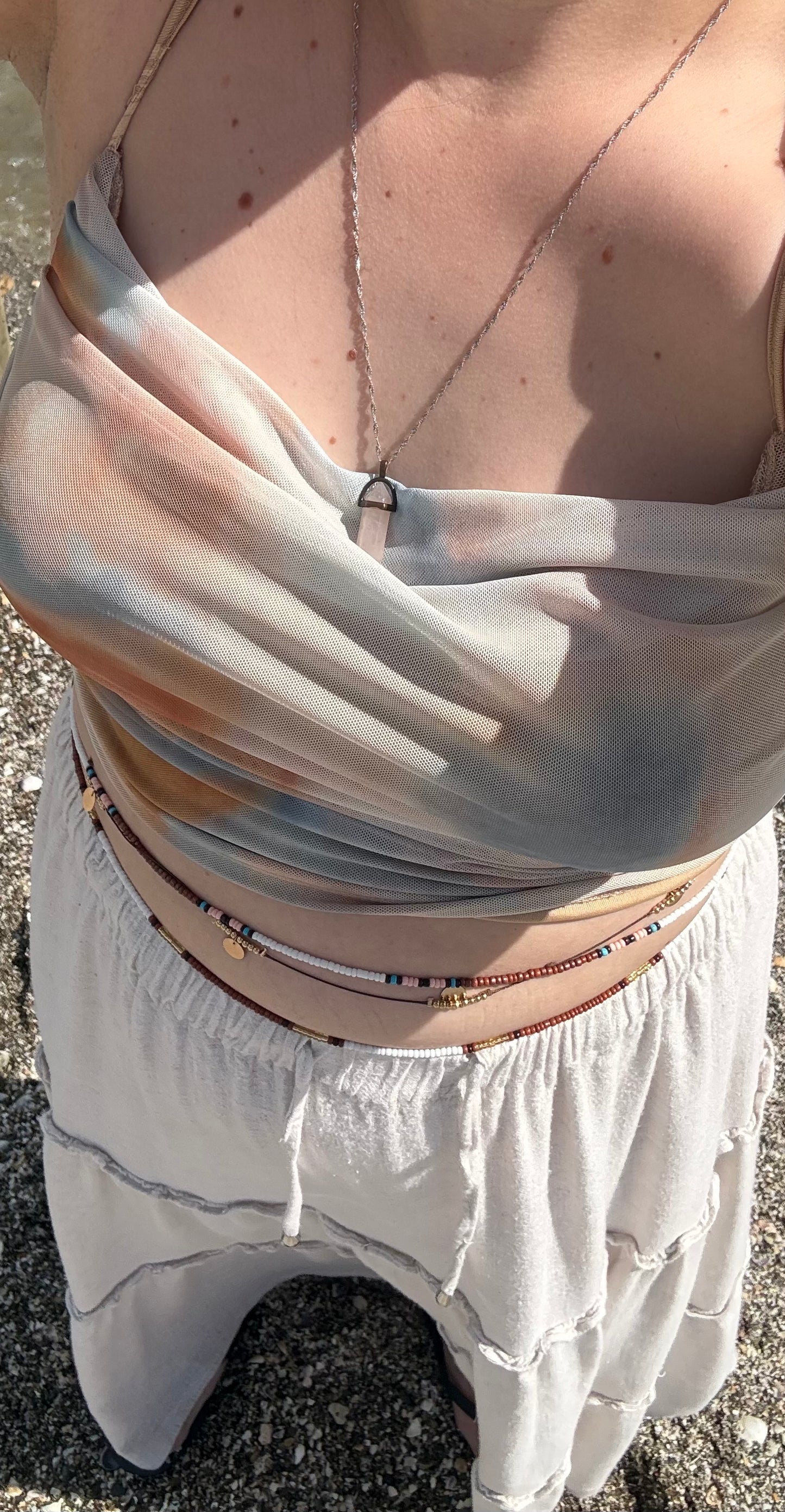 Beaded body chain worn across white dress waist, layered multicolor strands