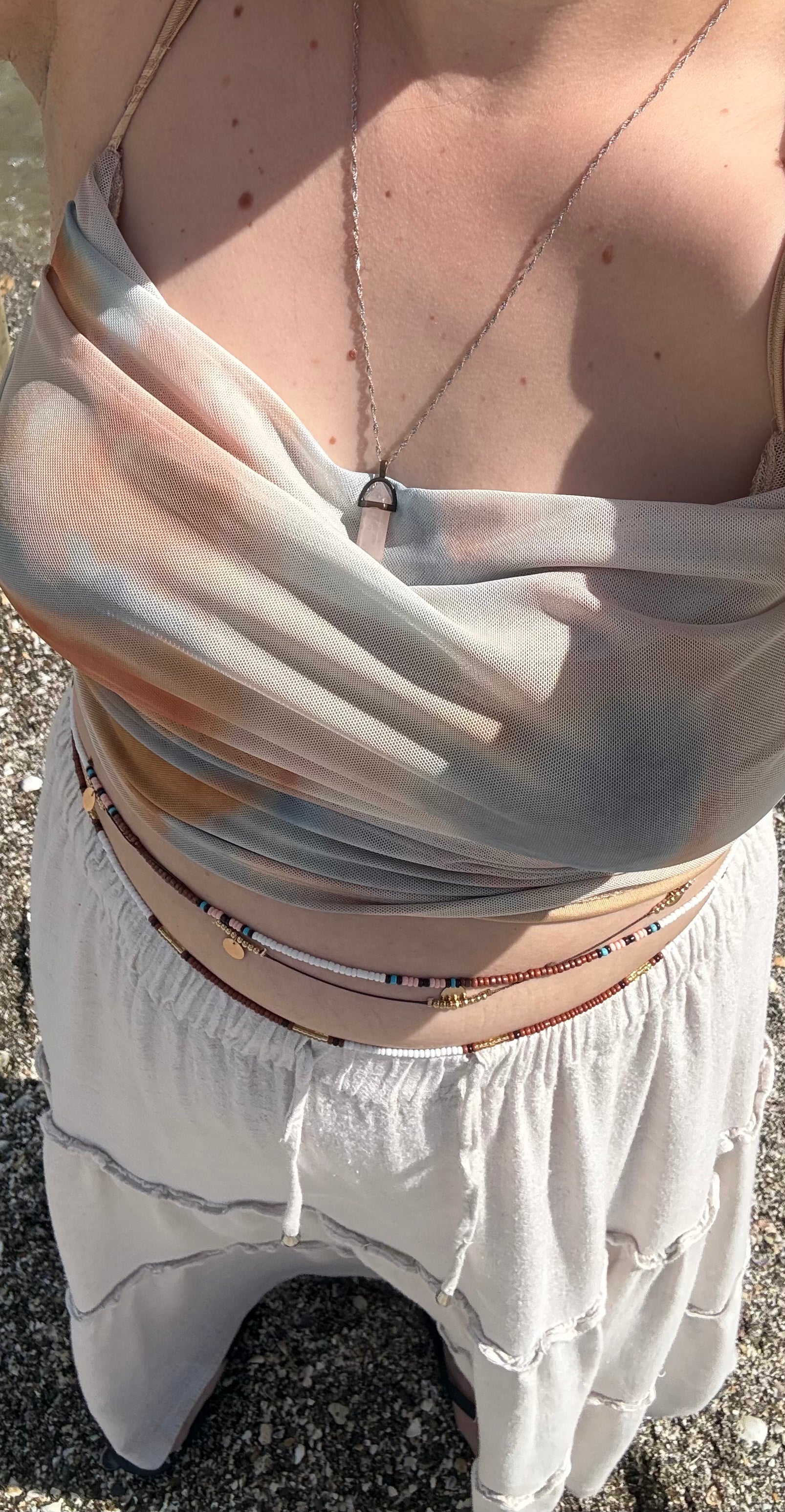 Beaded body chain worn across white dress waist, layered multicolor strands