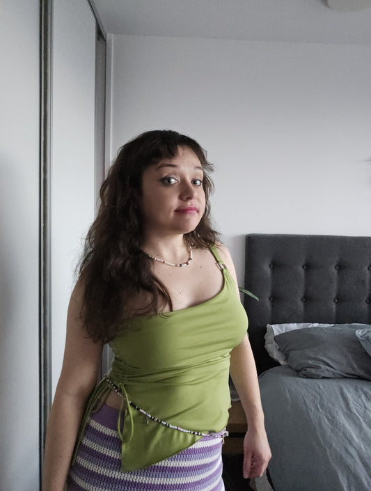 Woman in a green top standing in a bedroom with a bed and headboard in the background.