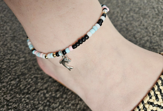 Beaded anklet with a bird charm on a person's ankle against a neutral background