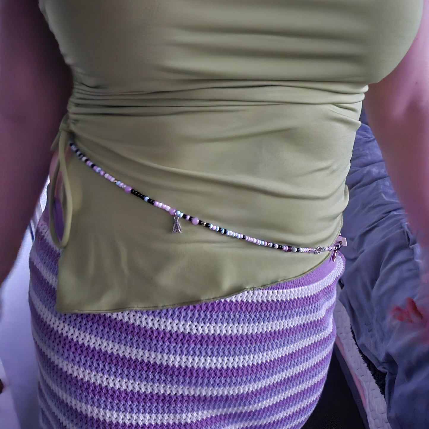 Close-up of a person wearing a green sleeve and a purple and white striped sweater with a bracelet.